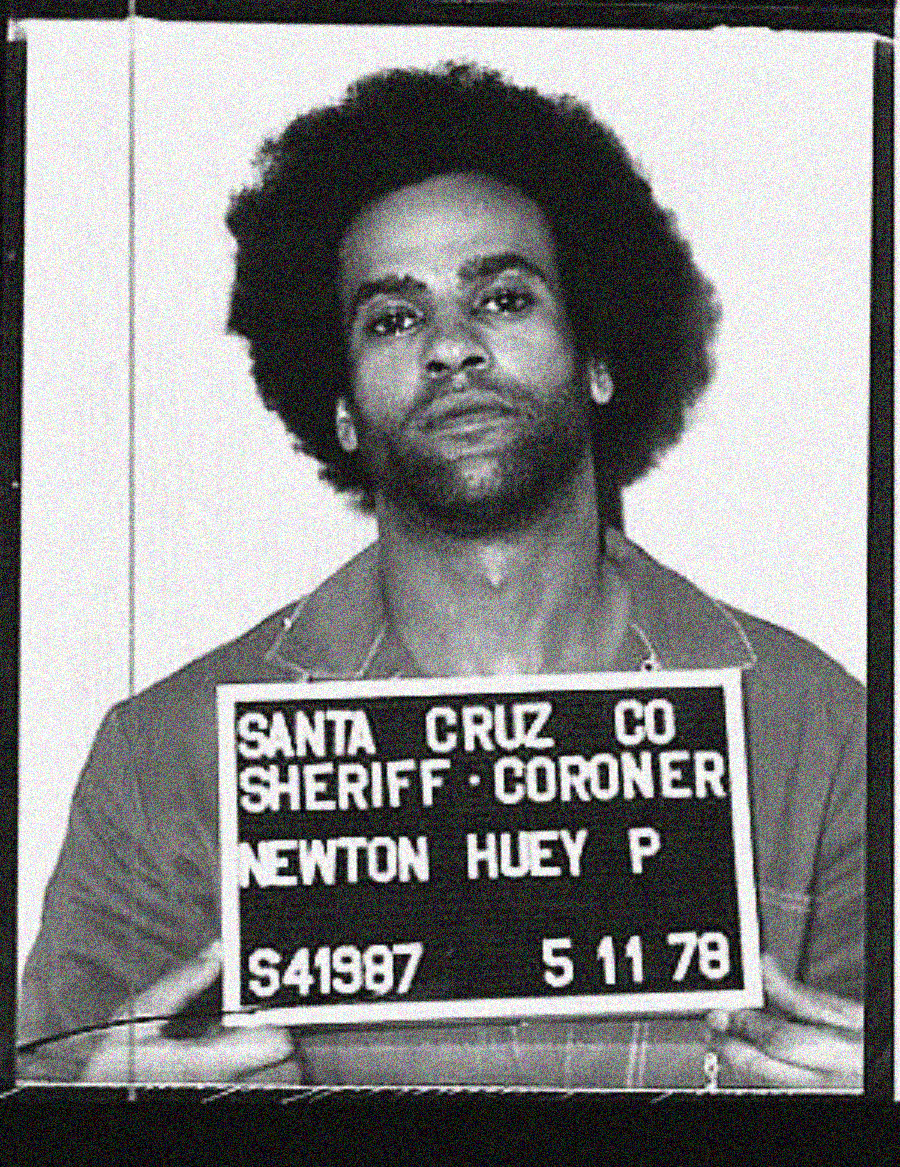 Black-and-white mugshot of a man holding a sign that reads "Santa Cruz Co Sheriff Coroner, Newton Huey P, S41987, 5 11 78." The man has an afro hairstyle and is wearing a collared shirt.