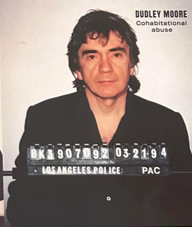 A man with dark hair wearing a dark jacket poses for a mugshot, holding a sign with numbers and "Los Angeles Police" written on it. Text in the top right corner says "Dudley Moore Cohabitational abuse.