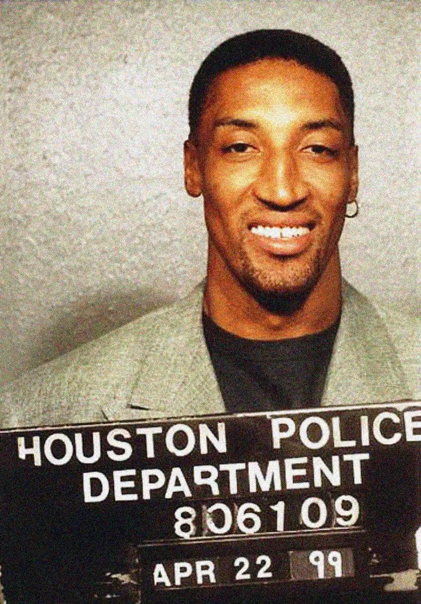 A man in a grey blazer smiles in a mugshot holding a sign that reads "Houston Police Department 806109" with the date "Apr 22 99" underneath.