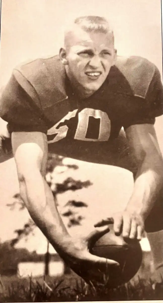 A vintage black-and-white photo of a football player in a uniform with the number 50, crouched and preparing to snap the ball, outdoors on a grassy field.
