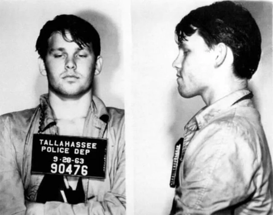 Black and white mugshot with front and side views of a young man in a jacket, holding a sign reading “Tallahassee Police Dept 9-28-63 90476.” The man has closed eyes and short dark hair.