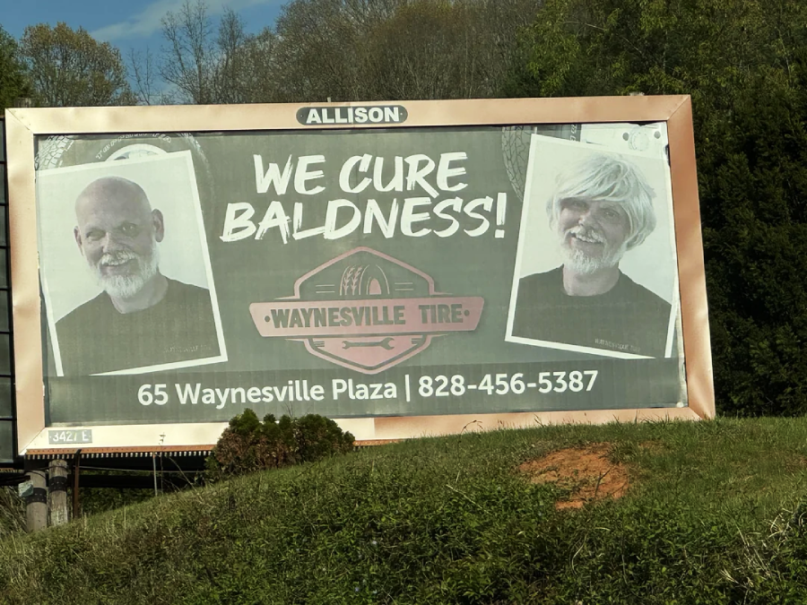 A billboard for Waynesville Tire shows two men, both smiling. The left image shows a bald man; the right image shows the same man with a full head of white hair. Text reads, "We cure baldness!" and gives the business's contact details.