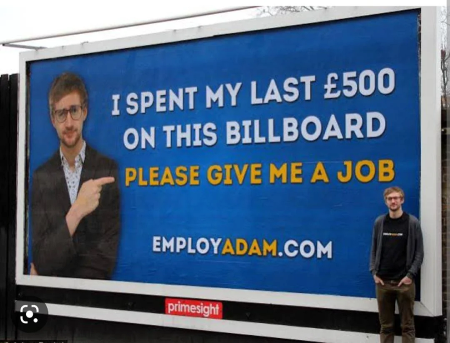A man stands next to a large billboard that reads, "I spent my last £500 on this billboard. Please give me a job. employadam.com" with his photo and him pointing to the text.