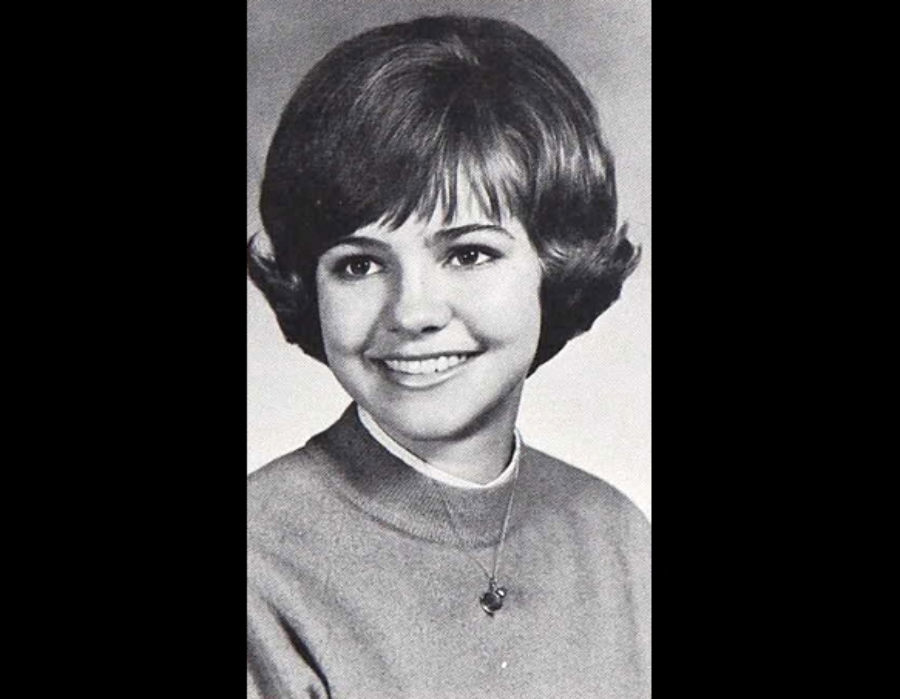 Black and white portrait of a young woman with short, styled hair, wearing a sweater and a necklace, smiling and looking slightly to the side.