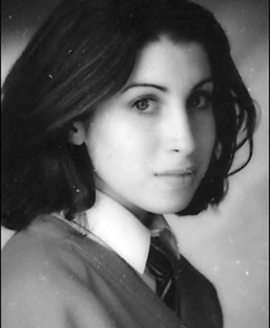 Black and white portrait of a young woman with shoulder-length dark hair, wearing a school uniform with a collared shirt, tie, and sweater, looking slightly to the side with a calm expression.