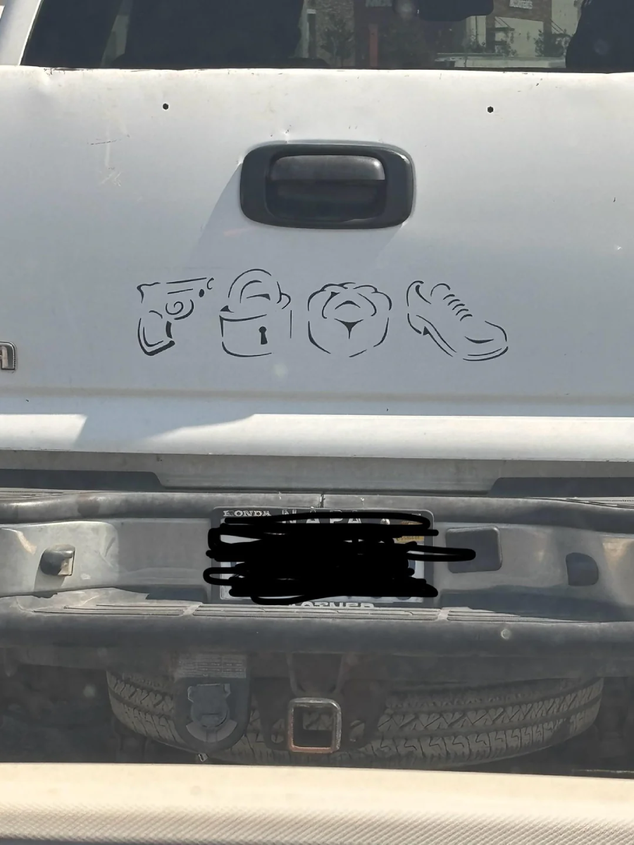 A white vehicle tailgate with a black decal showing a gun, a lock, a bear’s face, and a shoe, lined up in a row. The license plate below is scribbled out.