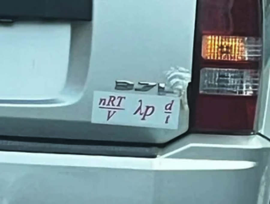 A bumper sticker on a silver SUV displays the ideal gas law and physics symbols written as: nRT/v, λp/d, and i, in red letters below the car’s emblem and right rear tail light.