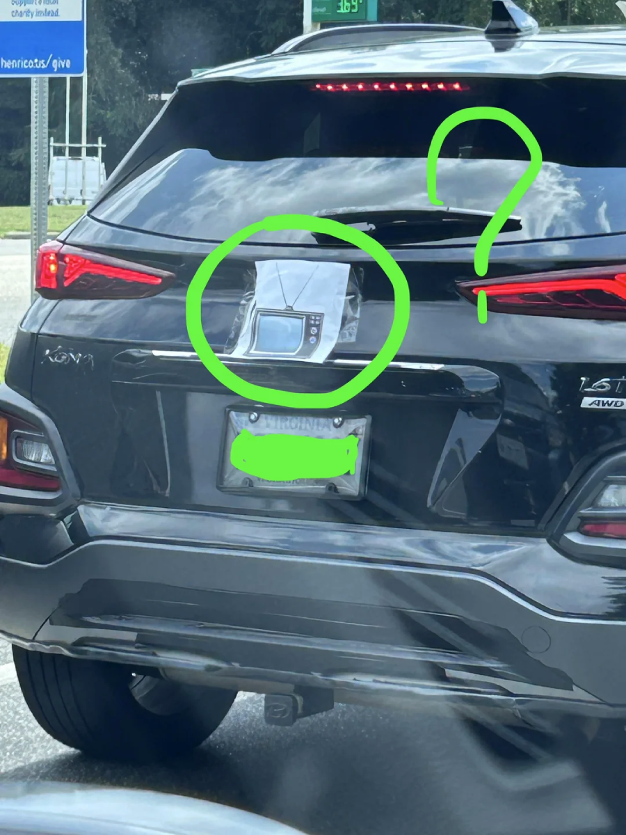 A photo of a black SUV with a small old TV set oddly attached to its rear hatch, circled in green with a large green question mark drawn next to it; the license plate is blurred.