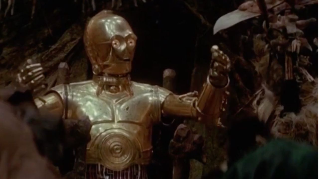 A shiny gold humanoid robot with raised arms stands among dark trees and branches, appearing surprised or expressive.