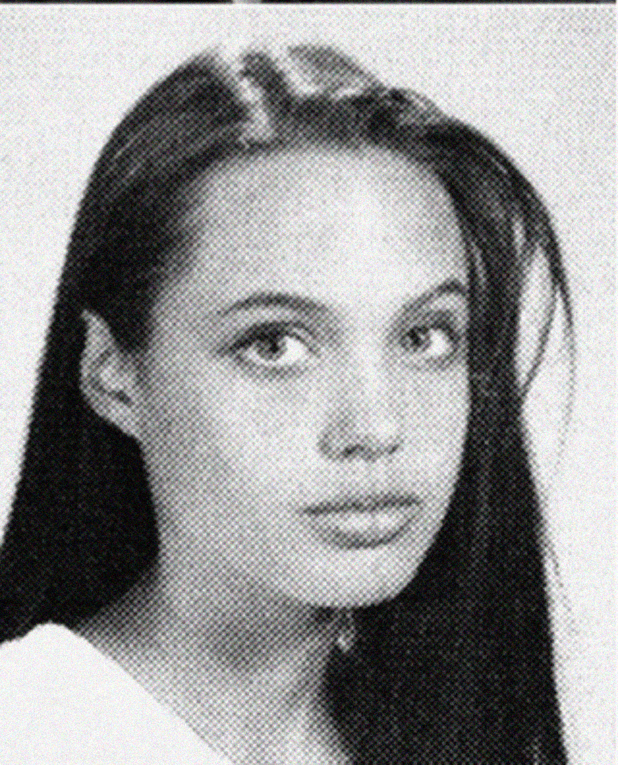 Black and white portrait of a young woman with long straight hair, parted in the center, looking directly at the camera with a neutral expression. She is wearing a light-colored top.
