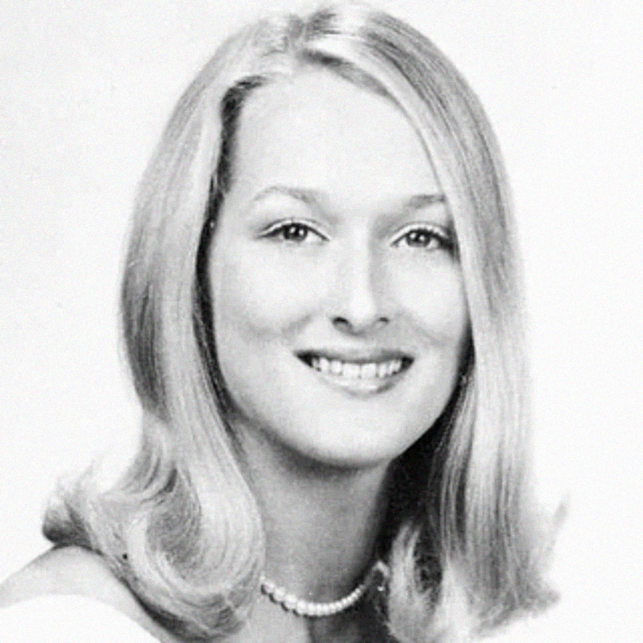 Black-and-white portrait of a young woman with light, shoulder-length hair, wearing a pearl necklace, a light off-the-shoulder top, and smiling at the camera.