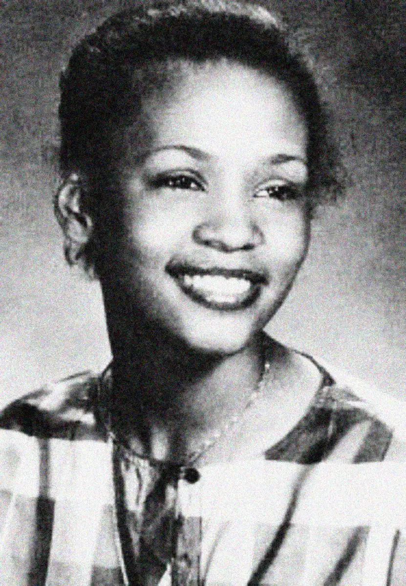 A young woman with short hair smiles, looking slightly off camera. She is wearing a plaid-patterned top and a necklace. The photo is black and white and appears to be a school portrait.