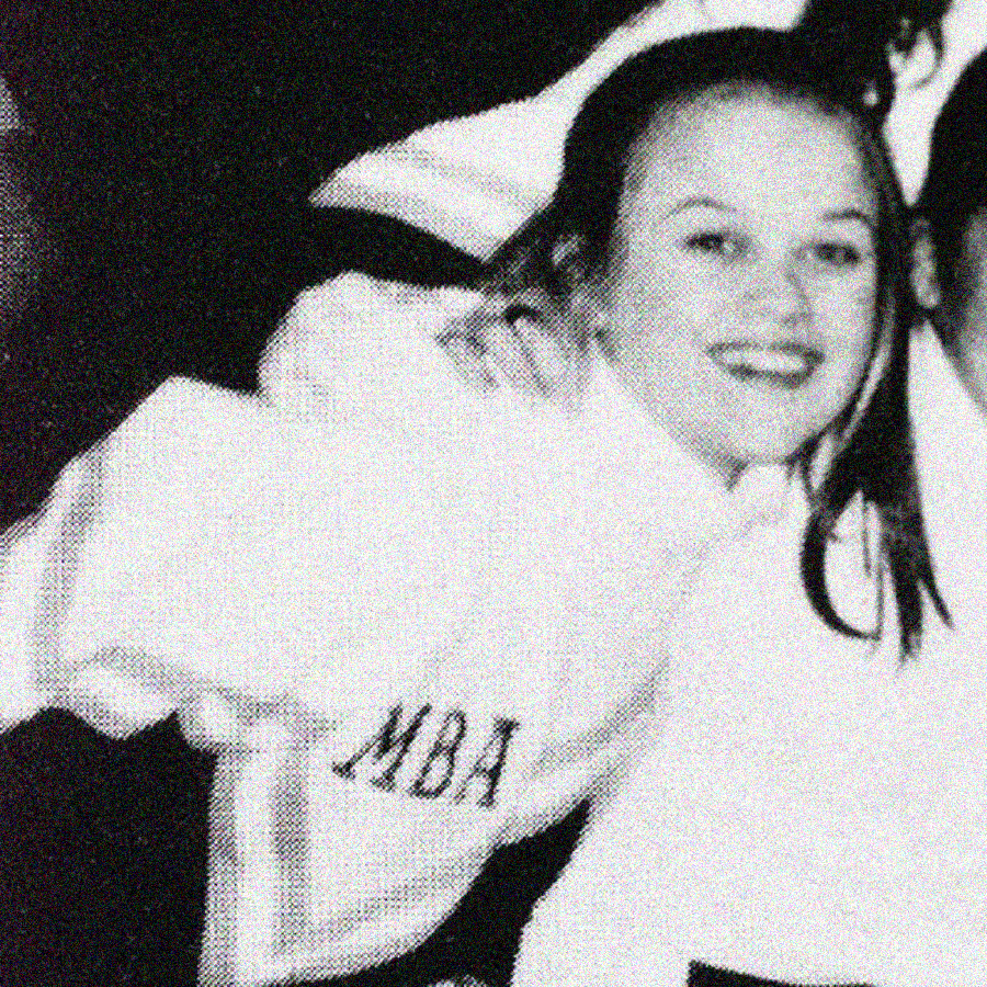 A young woman in a white sweater with "MBA" on the sleeve smiles at the camera in a black-and-white, grainy photo. She is leaning forward, and part of another person appears beside her.