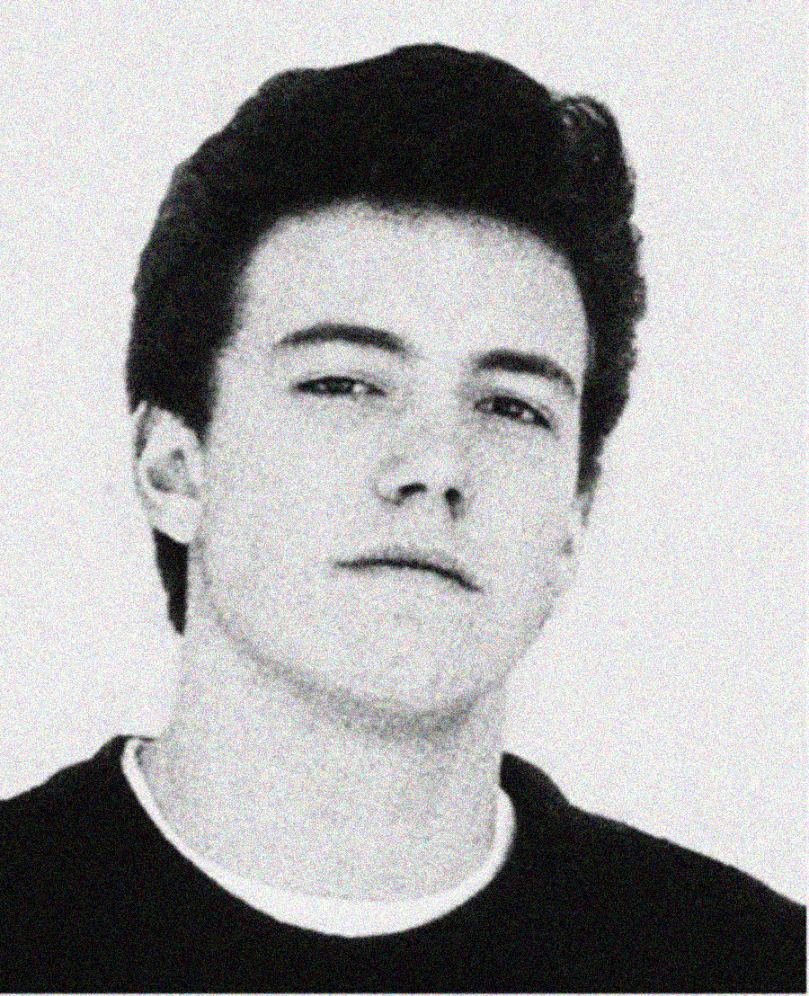 A black and white portrait of a young man with dark, styled hair, looking slightly up with a neutral expression. He is wearing a dark shirt and the background is plain and light-colored.