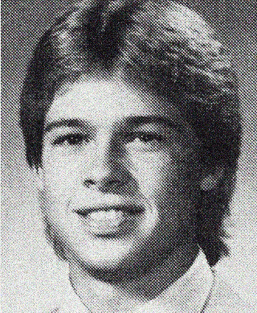 Black and white yearbook-style portrait of a young person with medium-length, feathered hair, smiling slightly and wearing a collared shirt and jacket.