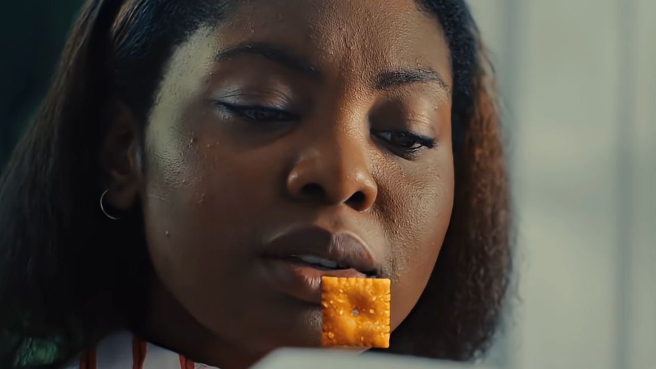 A woman holds a square cracker between her lips, looking down thoughtfully.