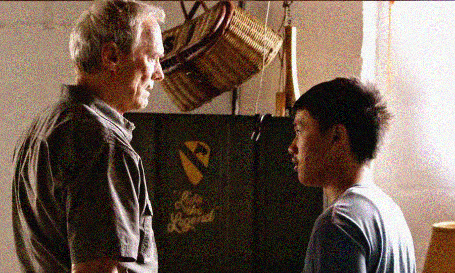 An older man and a younger man stand facing each other indoors, having a serious conversation. A basket and some objects hang on the wall behind them, and sunlight comes through a window on the right.