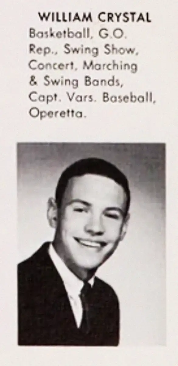 Black-and-white yearbook photo of a young man in a suit and tie with short hair, smiling. Text above lists his name, William Crystal, and his involvement in various school activities.