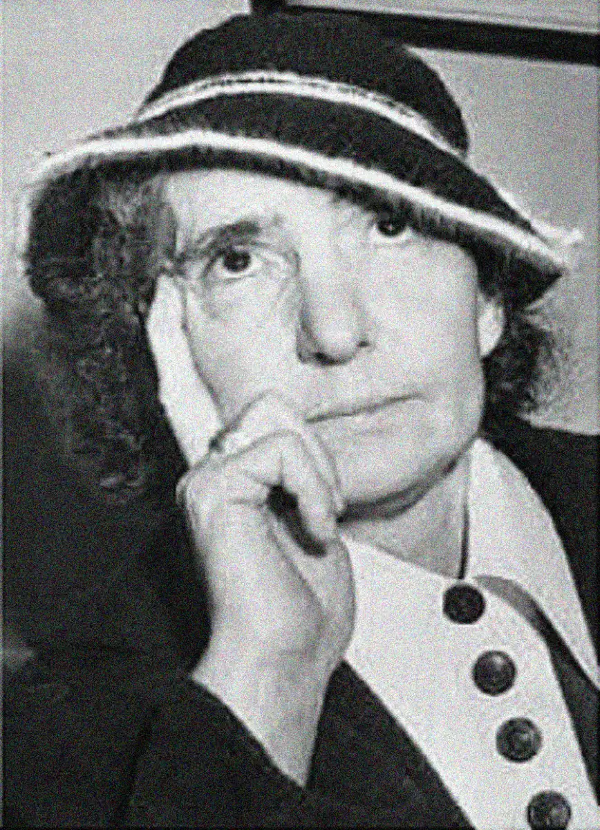 Black and white photo of a woman wearing a hat with a striped band, resting her face on her hand. She has a serious expression and is dressed in a collared coat with large buttons.