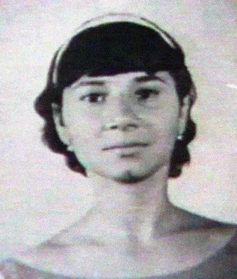 Black-and-white portrait of a young person with short, dark hair, wearing a headband and a simple, off-the-shoulder top, looking directly at the camera with a neutral expression.