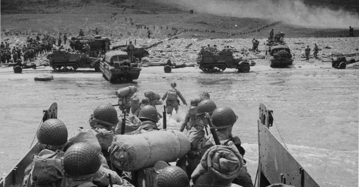 Soldiers wearing helmets and gear disembark from a landing craft onto a beach, with military vehicles and more troops visible in the background amid smoke and debris.