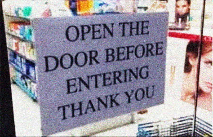 A sign on a glass door in a store reads: "OPEN THE DOOR BEFORE ENTERING THANK YOU." Shelves with products are visible in the background.