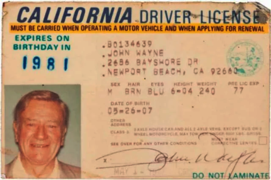 A worn California driver license featuring a smiling older man, John Wayne, with personal details, expiration date in 1981, and the signature "John Wayne" visible at the bottom right.