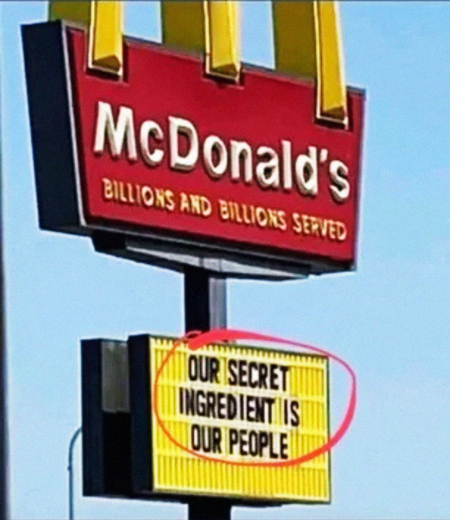 A McDonald’s sign reads, “OUR SECRET INGREDIENT IS OUR PEOPLE,” with the message circled in red under the main McDonald's billboard.