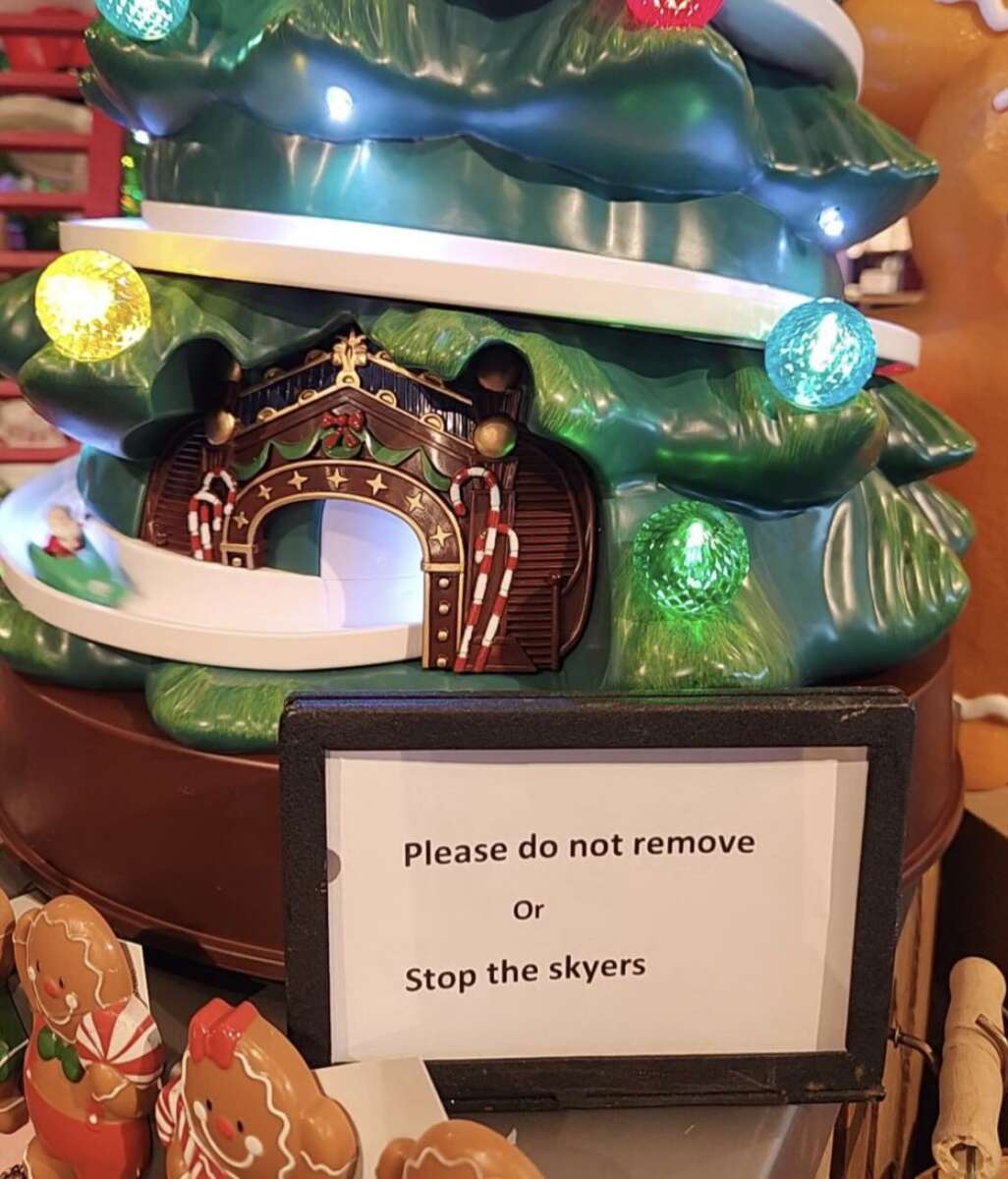 A sign reading "Please do not remove Or Stop the skyers" sits in front of a festive Christmas tree decoration with colorful lights and a gingerbread-themed entrance. Gingerbread figures are visible at the bottom.