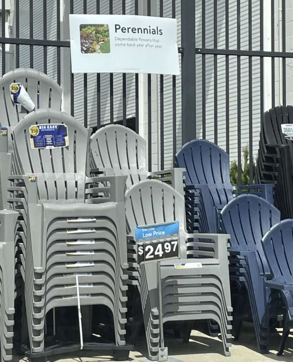 Stacks of gray and blue plastic lawn chairs are displayed for sale outside. Above them is a sign for perennials, which seems unrelated to the chairs. One stack of chairs is priced at $24.97.