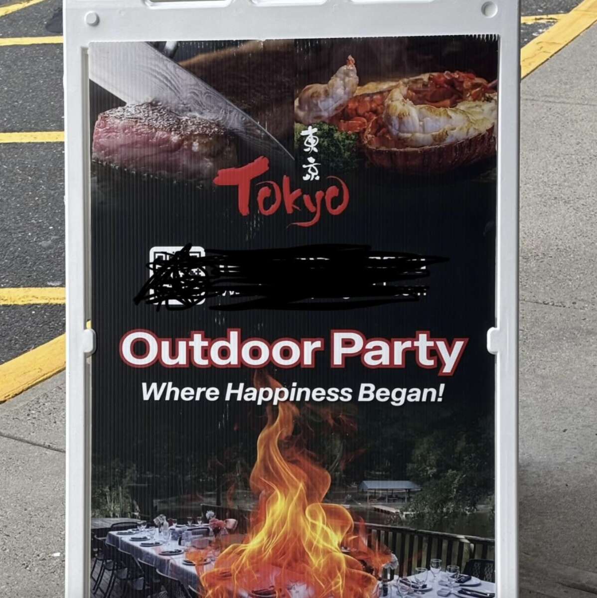 A sign for Tokyo restaurant advertises an outdoor party with the slogan "Where Happiness Began!" It shows grilled steak, lobster, a flaming grill, and a set outdoor dining table.