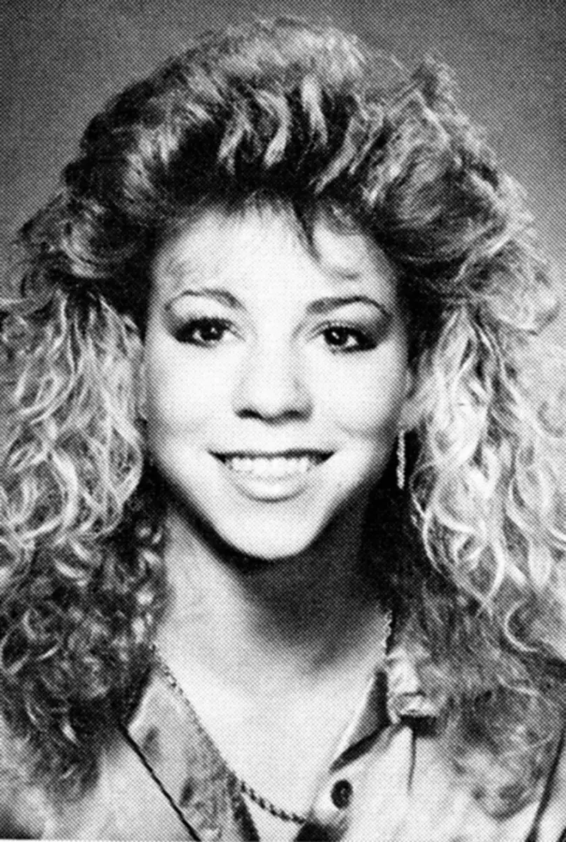 Black and white portrait of a young woman with voluminous curly hair, smiling at the camera and wearing a collared shirt and a necklace.