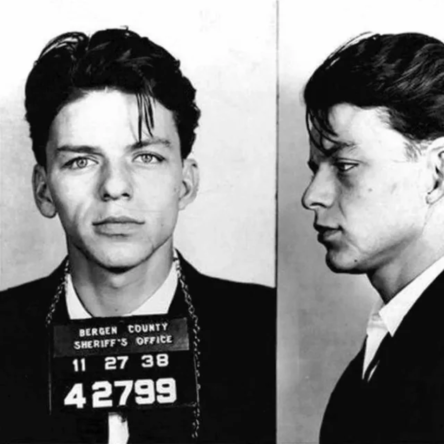 Black and white mugshot showing a young man in a suit with slicked hair, facing forward and in profile. He holds a placard reading “Bergen County Sheriff’s Office” with the date 11-27-38 and number 42799.