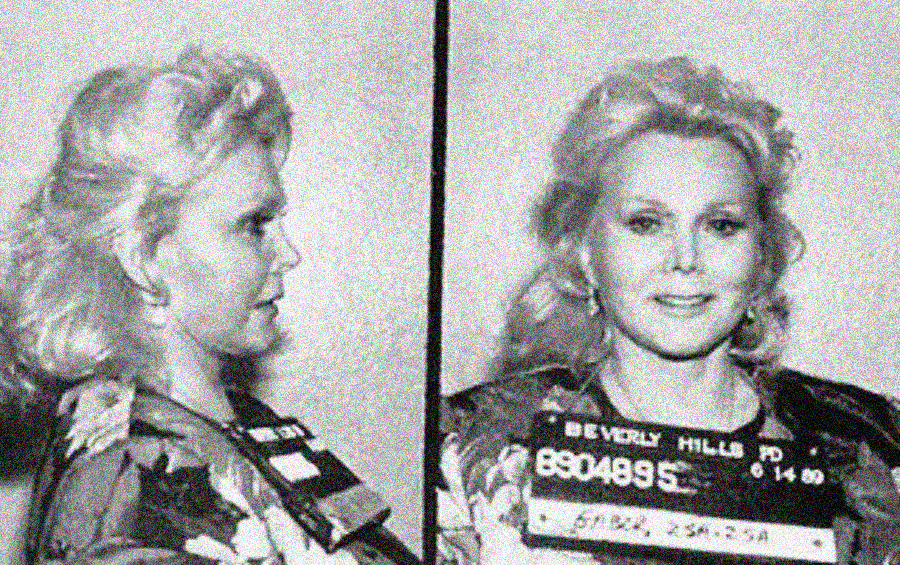 Black-and-white mugshot of a woman with blonde hair, seen in profile and facing forward, holding an identification board labeled "Beverly Hills PD." She is wearing a floral-patterned top.