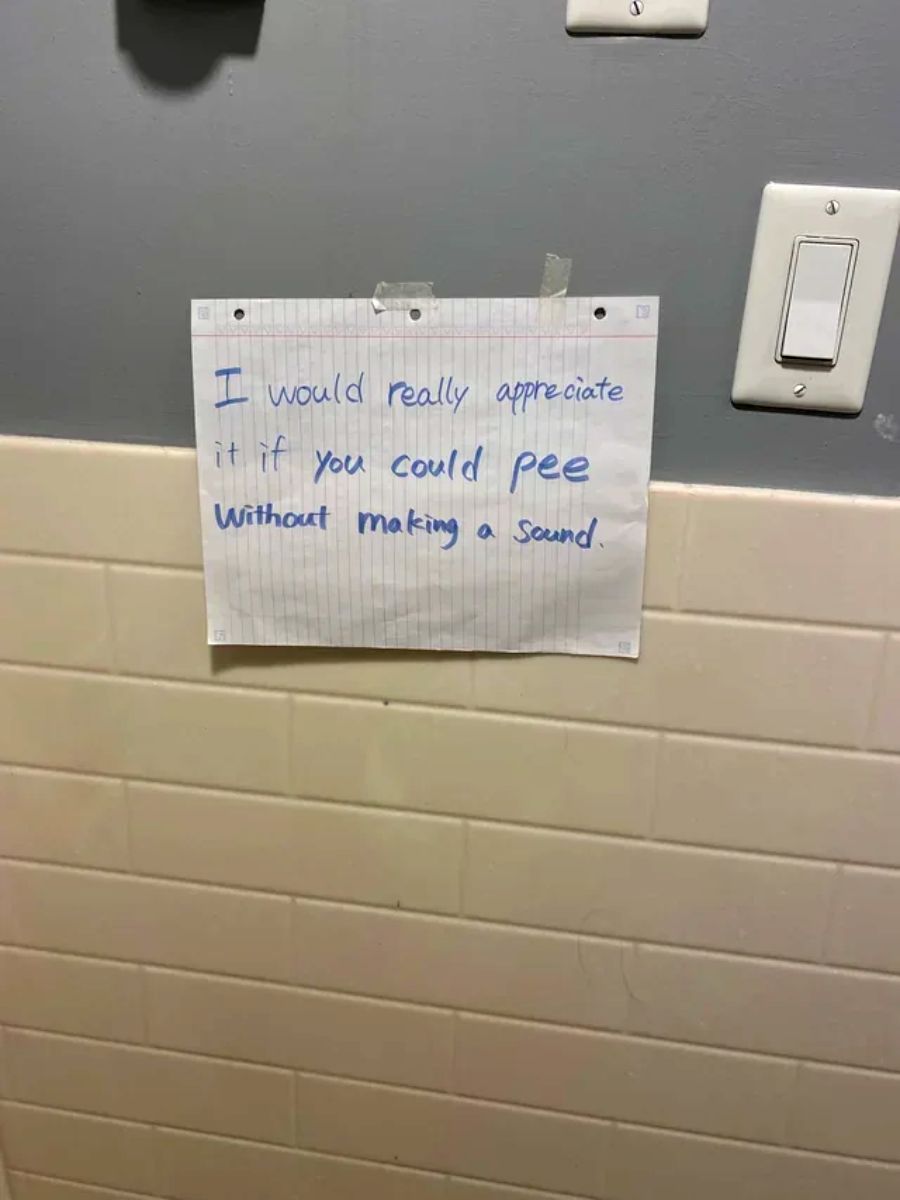 A handwritten note taped to a bathroom wall reads: "I would really appreciate it if you could pee without making a sound." The note is written in blue ink on lined paper.