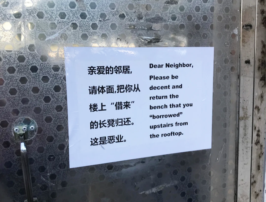 A printed note in Chinese and English is taped to a metal surface, asking a neighbor to return a “borrowed” bench that was taken from the rooftop.