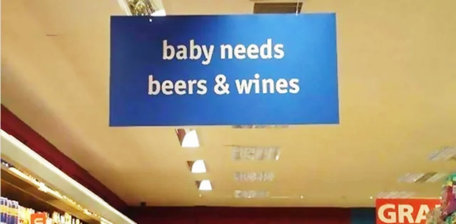 A blue grocery store sign reads "baby needs beers & wines," suggesting an amusing and confusing mix-up in aisle labeling.