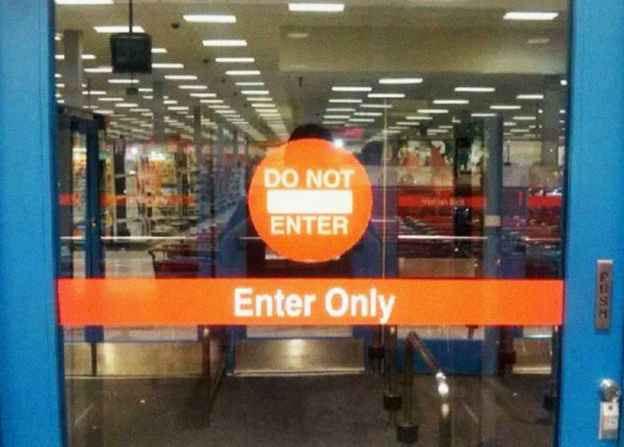 A glass door with a red "DO NOT ENTER" sign above another red sign stating "Enter Only," creating a confusing message. The interior of a brightly-lit store is visible through the door.