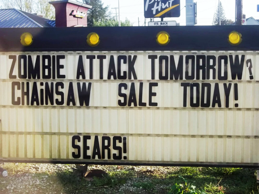A sign reads: "Zombie attack tomorrow? Chainsaw sale today! Sears!" with a Pizza Hut sign visible in the background.