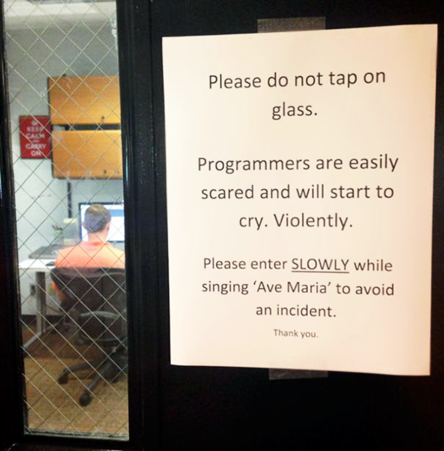 A sign on a door reads: "Please do not tap on glass. Programmers are easily scared and will start to cry. Violently. Please enter SLOWLY while singing 'Ave Maria' to avoid an incident. Thank you.