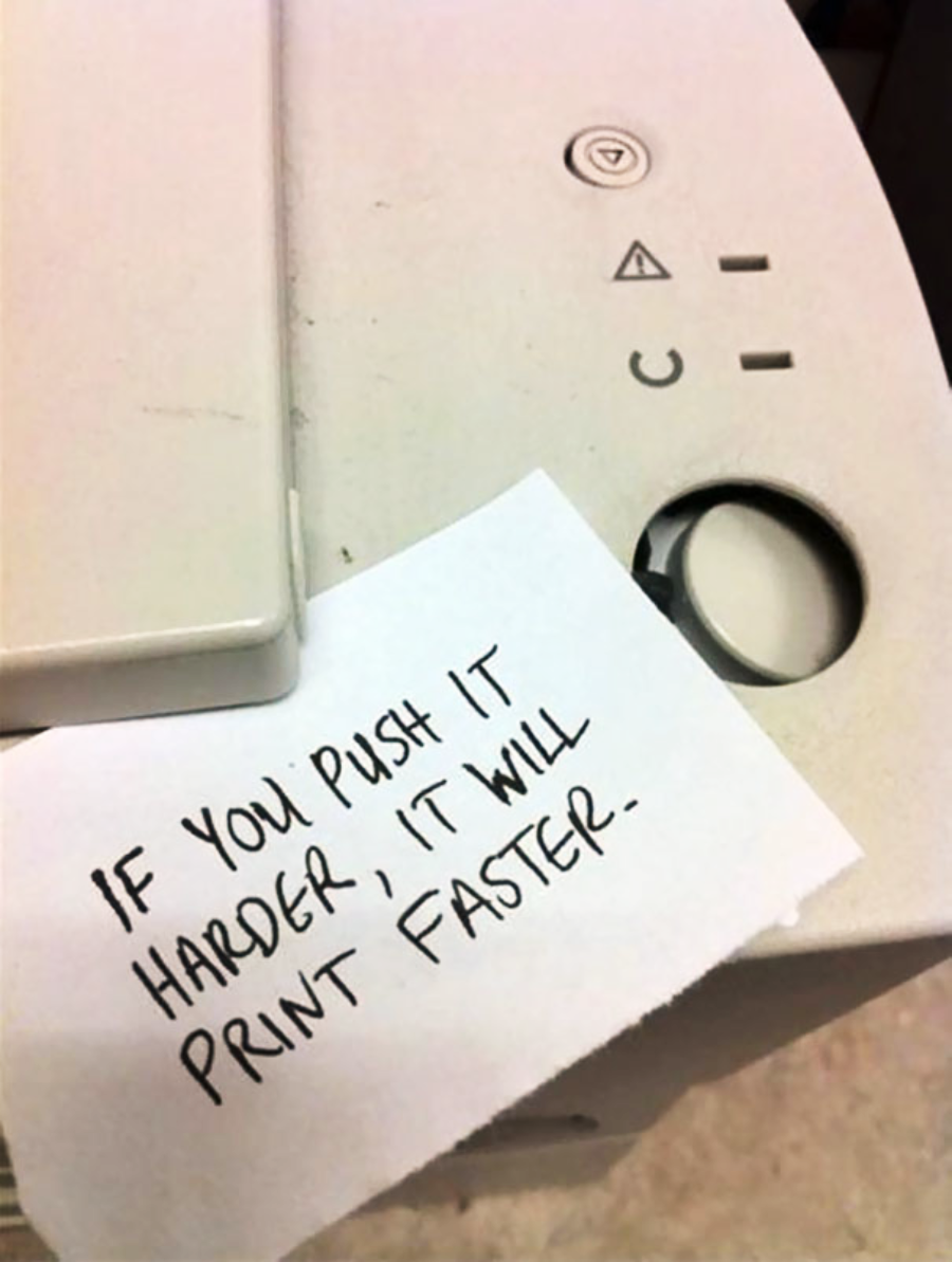 A handwritten note on a printer reads, "IF YOU PUSH IT HARDER, IT WILL PRINT FASTER." The note is placed next to the printer’s power and control buttons.
