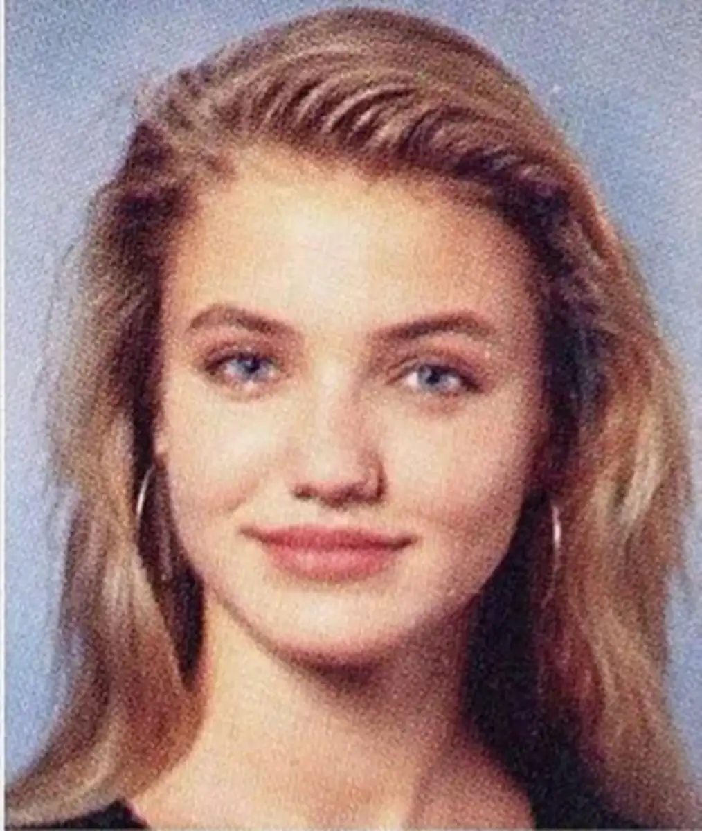 A young woman with long blonde hair, blue eyes, and hoop earrings smiles slightly at the camera against a plain, gradient blue background.