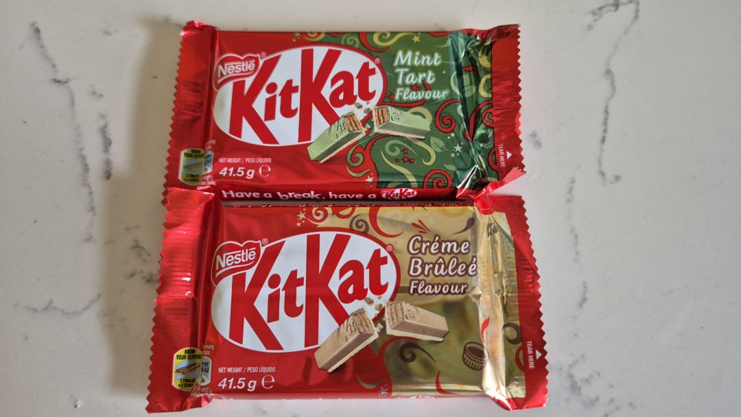 Two Nestlé KitKat bars on a white surface: the top one is mint tart flavour in green packaging, the bottom one is crème brûlée flavour in gold packaging. Both bars weigh 41.5 grams.
