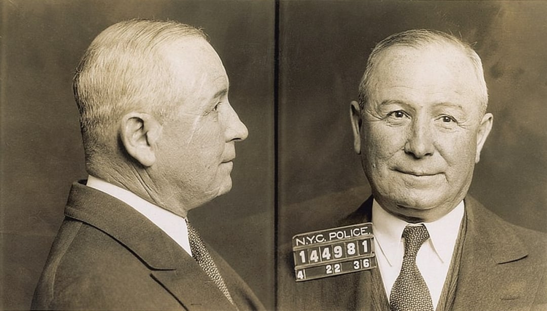 Vintage mugshot of an older man in a suit and tie, shown in both profile and front-facing views, holding a placard with "N.Y.C. Police" and identification numbers.