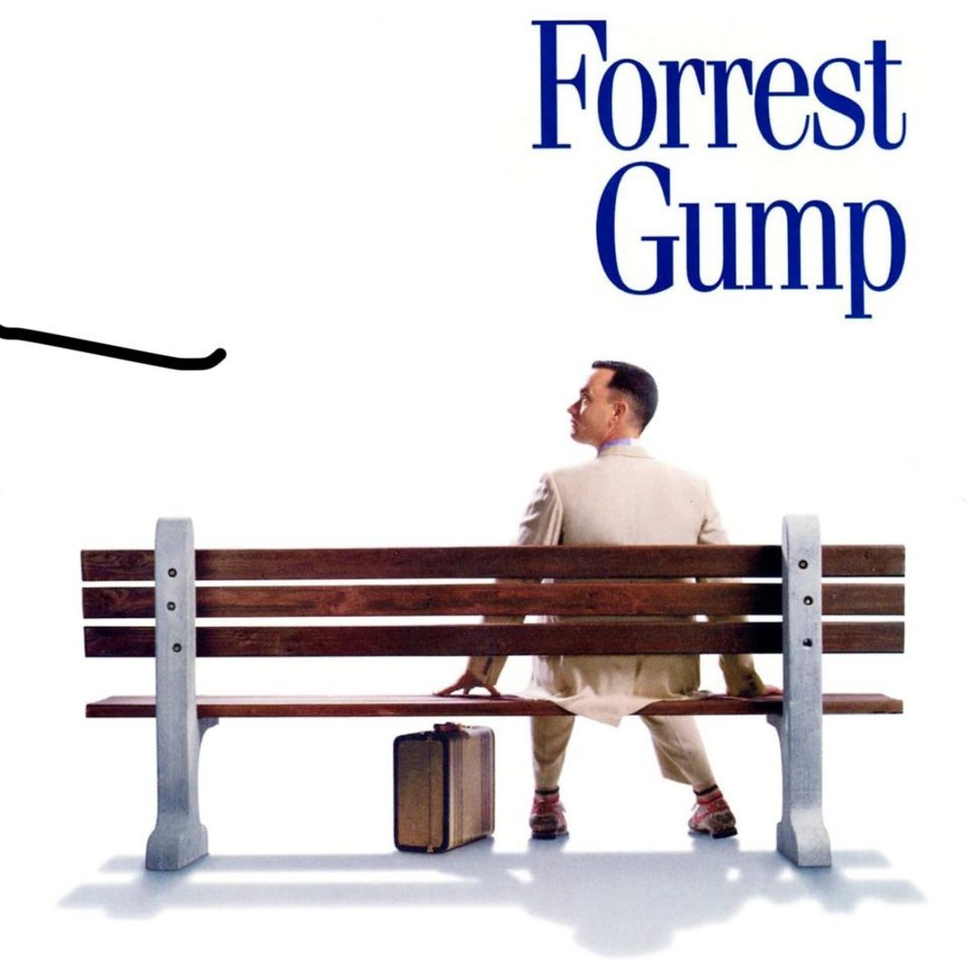 A man in a light suit sits on a wooden bench with a suitcase at his feet, looking to the right. The text above reads "Forrest Gump" in large blue letters on a plain white background.
