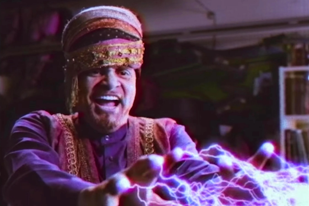 A man in a colorful turban and robe smiles widely while purple lightning bolts shoot from his outstretched fingertips in a dramatic, magical scene.