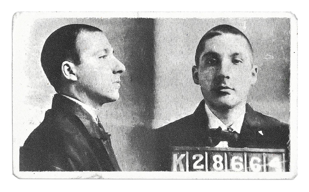 Black and white mugshot of a man with short hair, shown in profile and front view, wearing a suit. He holds a placard with the numbers K28664. The image has a vintage, worn appearance.