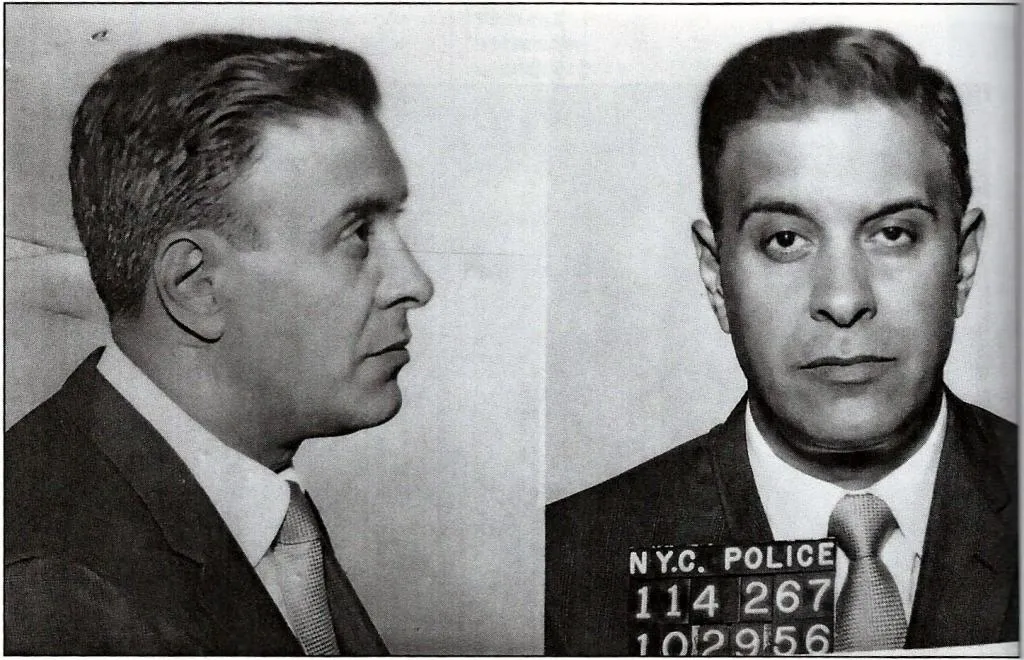 Black-and-white mugshot of a man in a suit and tie, shown in both profile and front views, with an identification board reading "N.Y.C. POLICE 114267 10 29 56.