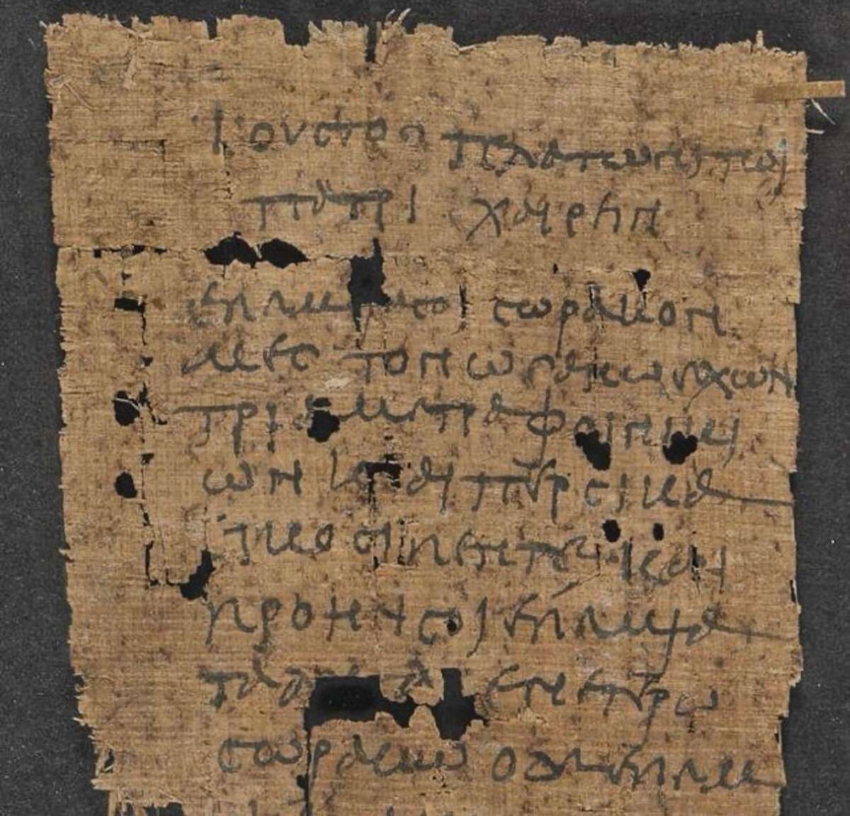 A worn, ancient piece of papyrus with Greek text written in faded black ink. The papyrus has several holes, torn edges, and sits on a dark background.