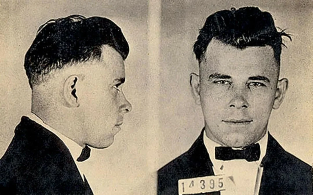Black-and-white mugshot showing a man in a suit and bow tie. The image displays both a side profile and a front view. He has short dark hair and holds a placard with the number 14395.
